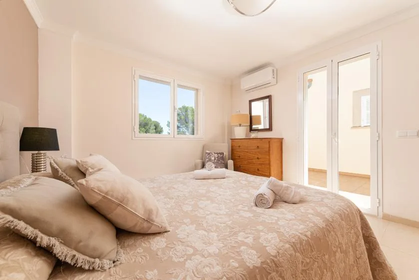 A bright bedroom with a bed, a window, and a wooden dresser.