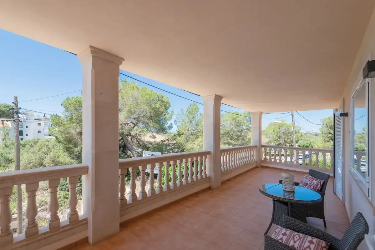 A covered terrace with railing, outdoor seating, and views of trees.