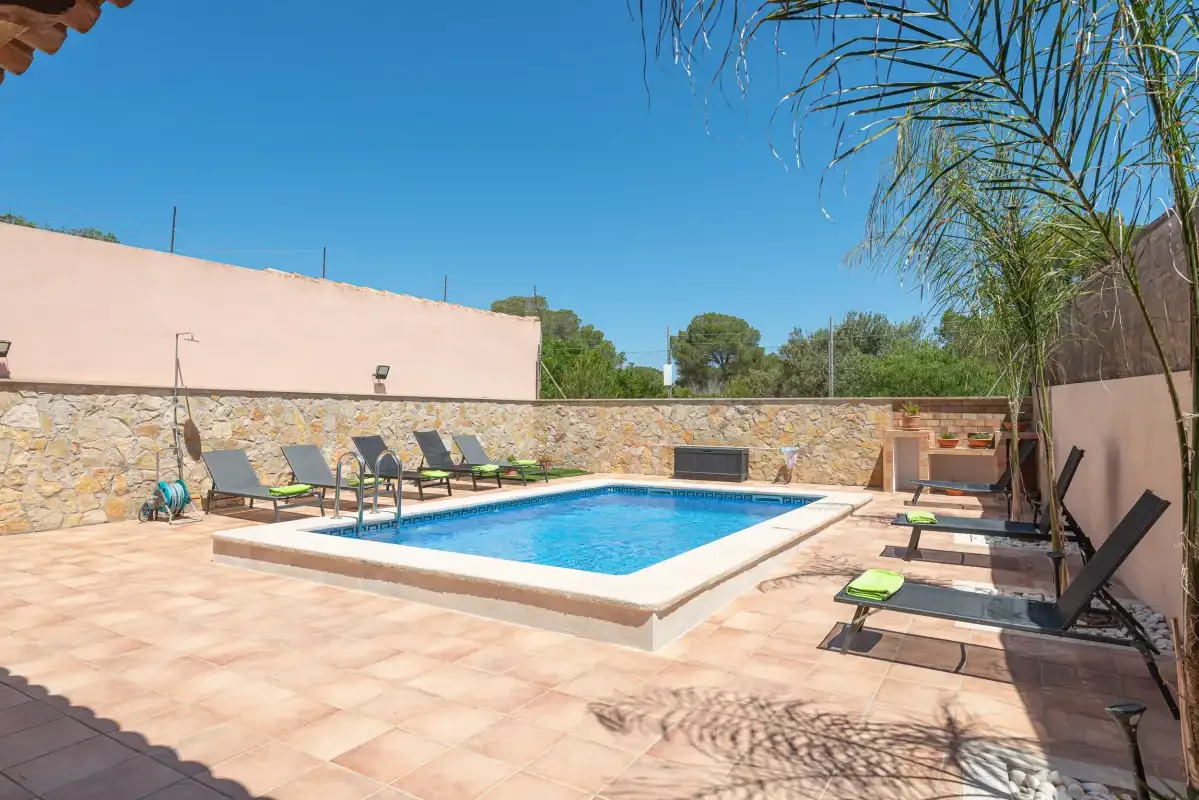 An outdoor swimming pool is surrounded by tiled paving and lounge seating.