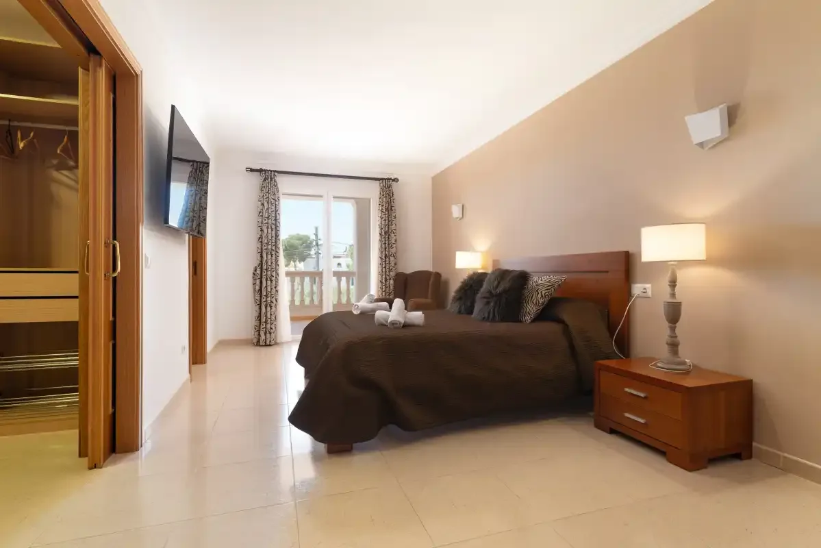A bedroom with a bed, bedside tables, and a glass door opening to a balcony.
