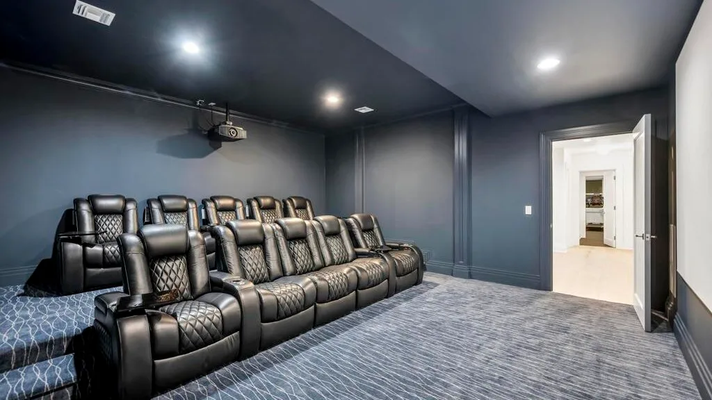 Una sala de cine en casa con filas de asientos reclinables oscuros y un proyector.