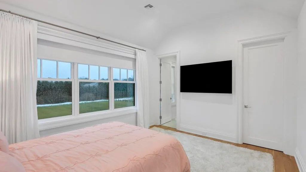 Un dormitorio con una ventana grande y un televisor montado en la pared.