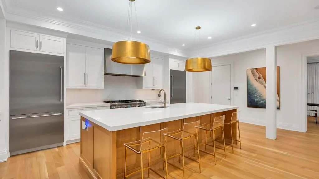 Una cocina moderna y luminosa con una isla grande y lámparas colgantes doradas.