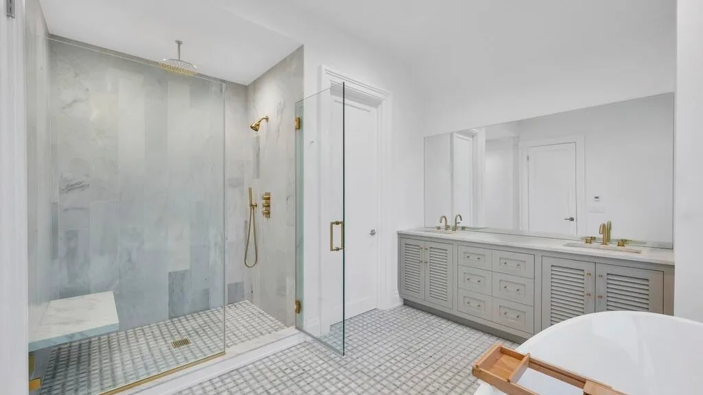 Un baño luminoso tiene una ducha de vidrio y un tocador largo con espejo.