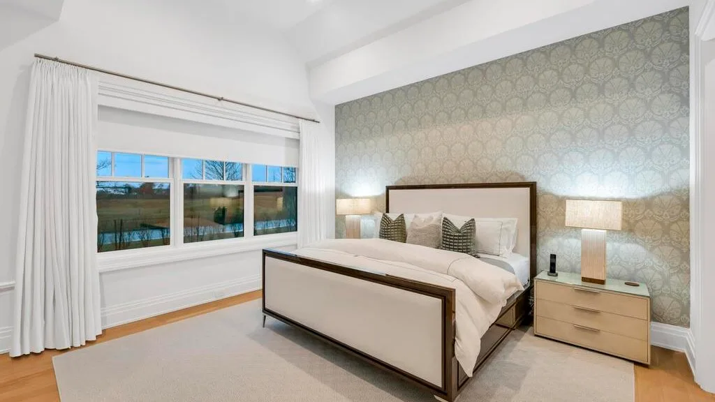 Un dormitorio luminoso con una cama, una pared decorativa estampada y ventanas amplias.