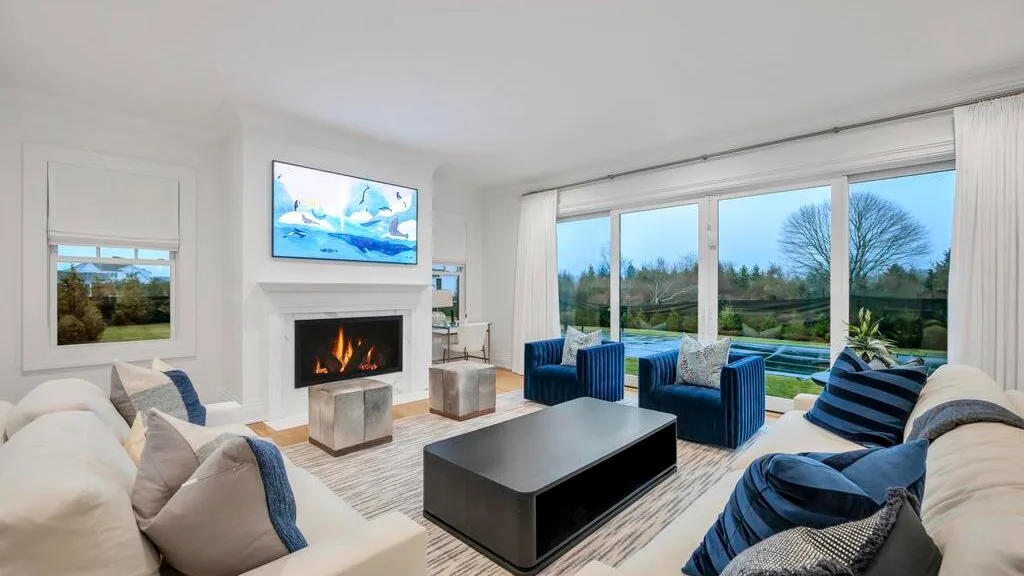 Una sala luminosa con chimenea, asientos y grandes ventanas con vistas a la vegetación.