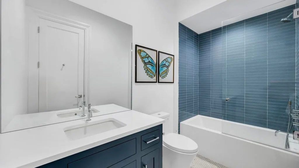 Un baño luminoso con lavabo blanco, inodoro y bañera junto a azulejos azules.