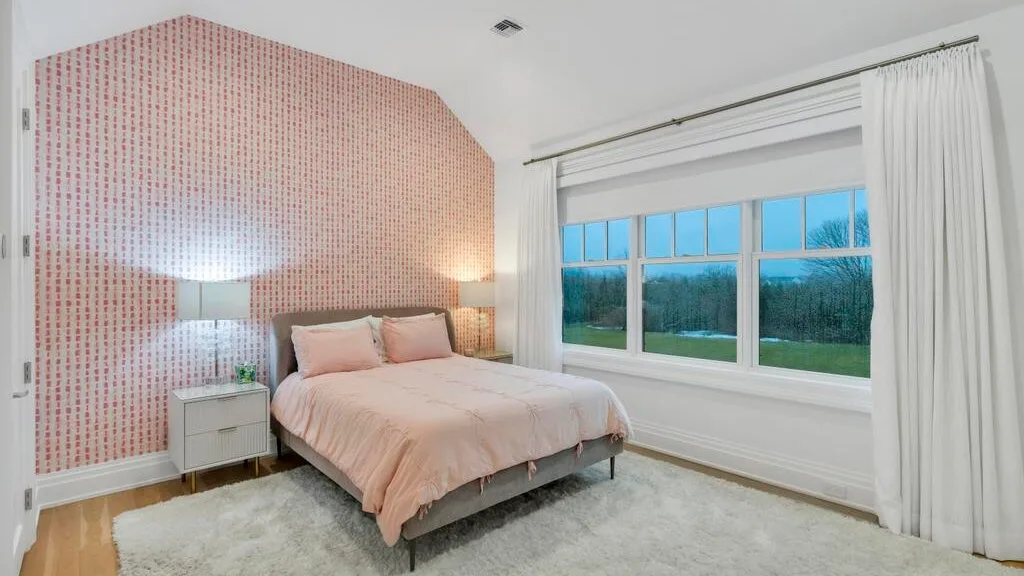 Un dormitorio con una cama junto a una ventana amplia que da a una zona de césped.
