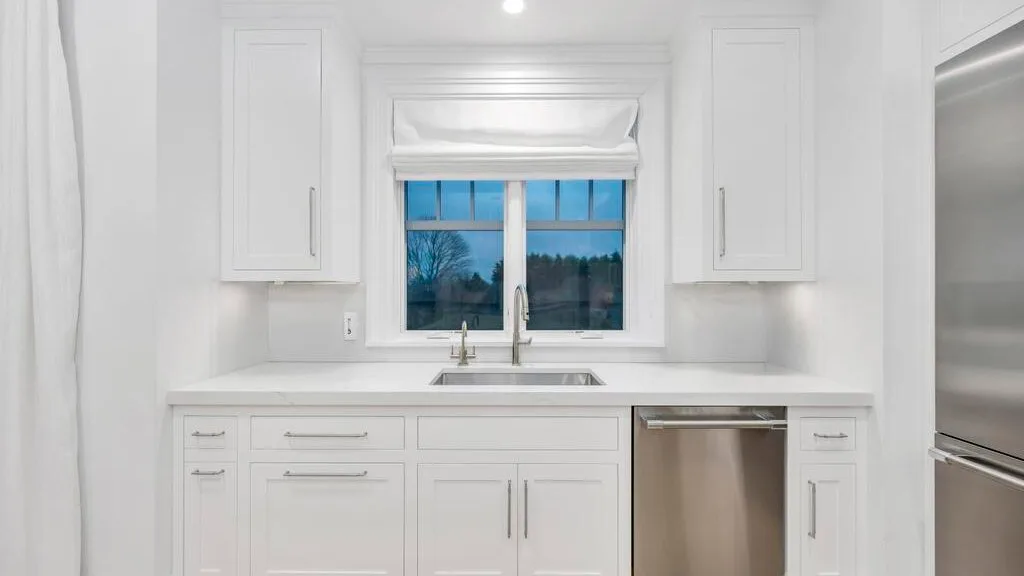 Una cocina blanca y luminosa con un fregadero bajo una ventana.