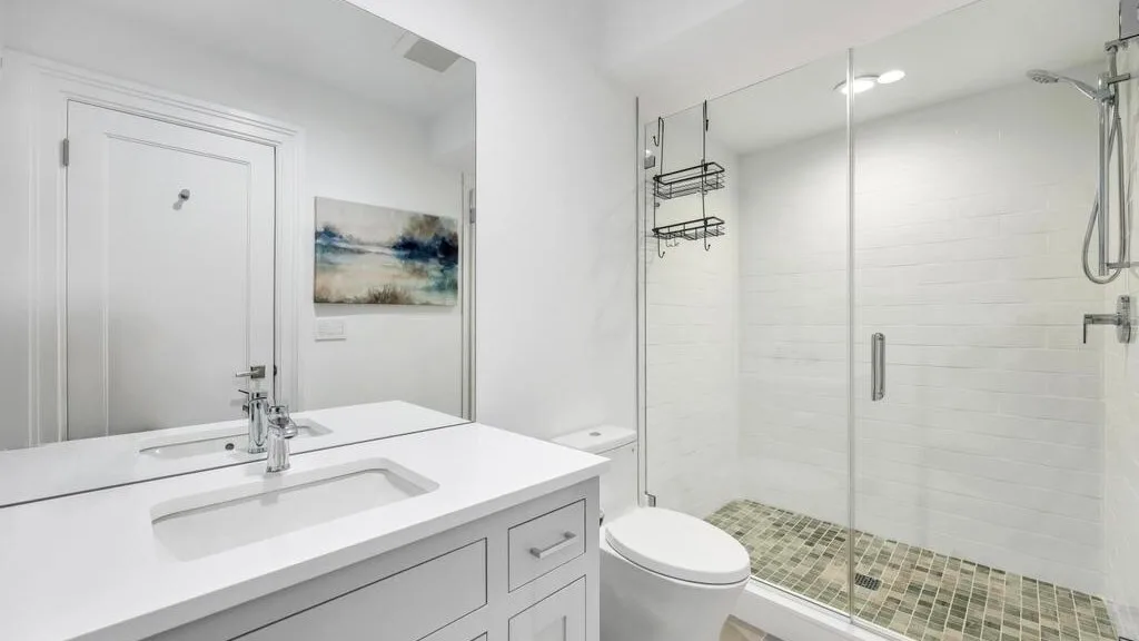 Un baño luminoso con tocador, inodoro y ducha con mampara de vidrio.