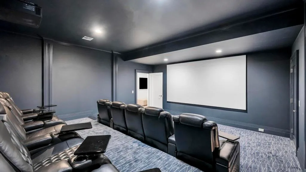 Una sala de cine en casa con asientos reclinables frente a una gran pantalla de proyección.