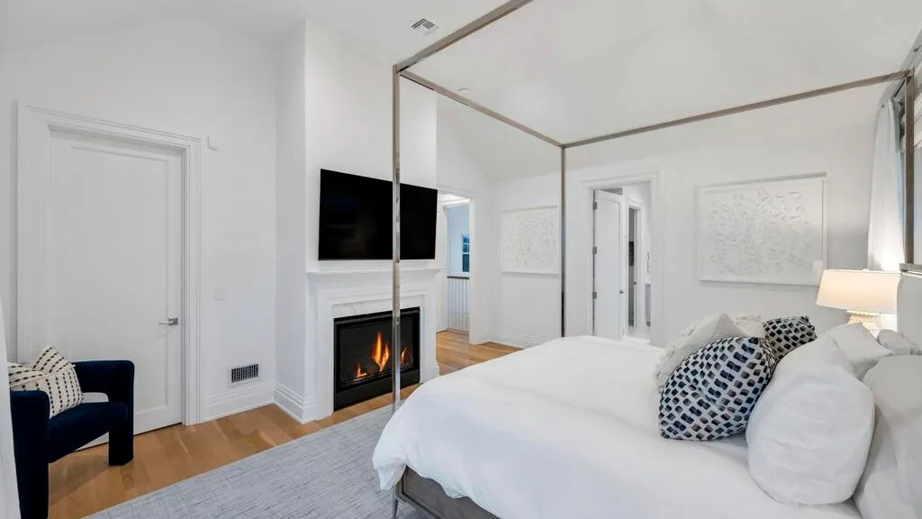 Un dormitorio luminoso con una cama blanca, una chimenea y un televisor.