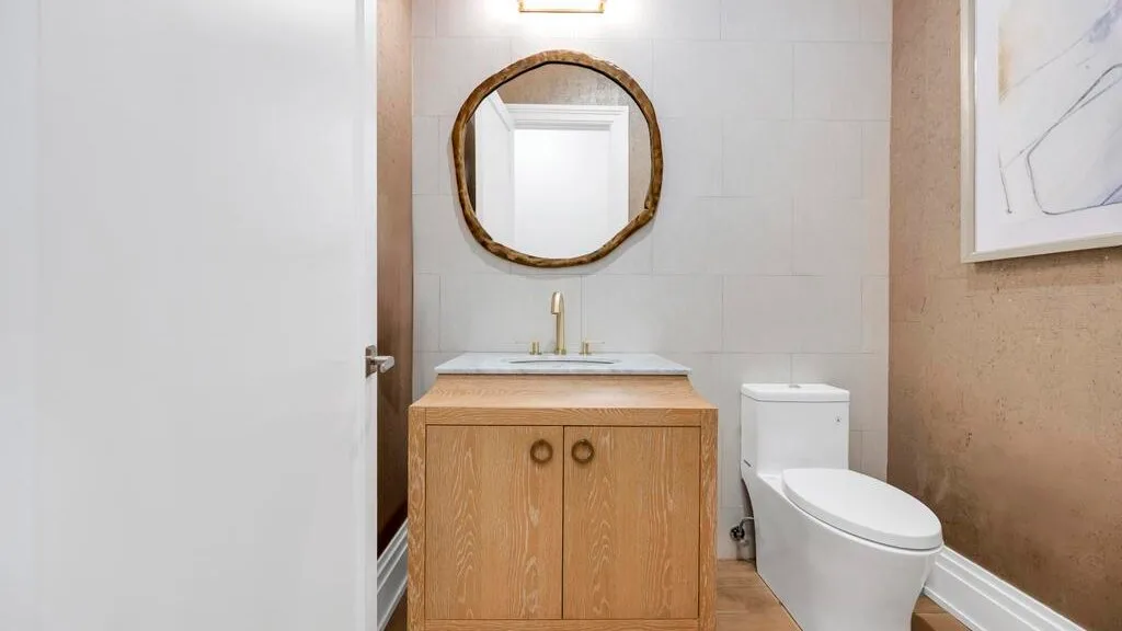 Un baño con un tocador de madera, un espejo redondo y un inodoro.