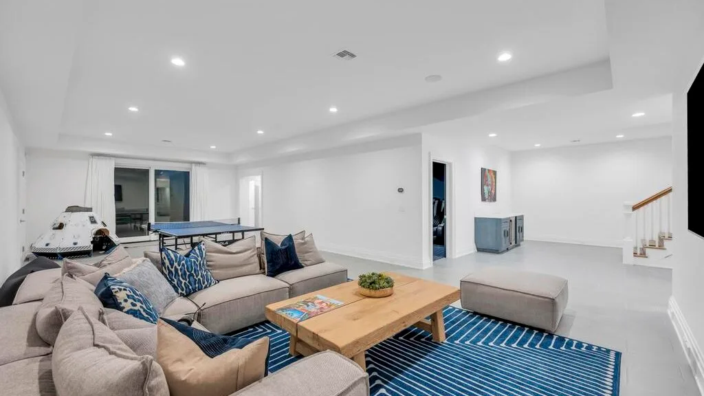 Una sala de estar luminosa con asientos alrededor de una mesa de centro de madera y una alfombra azul.