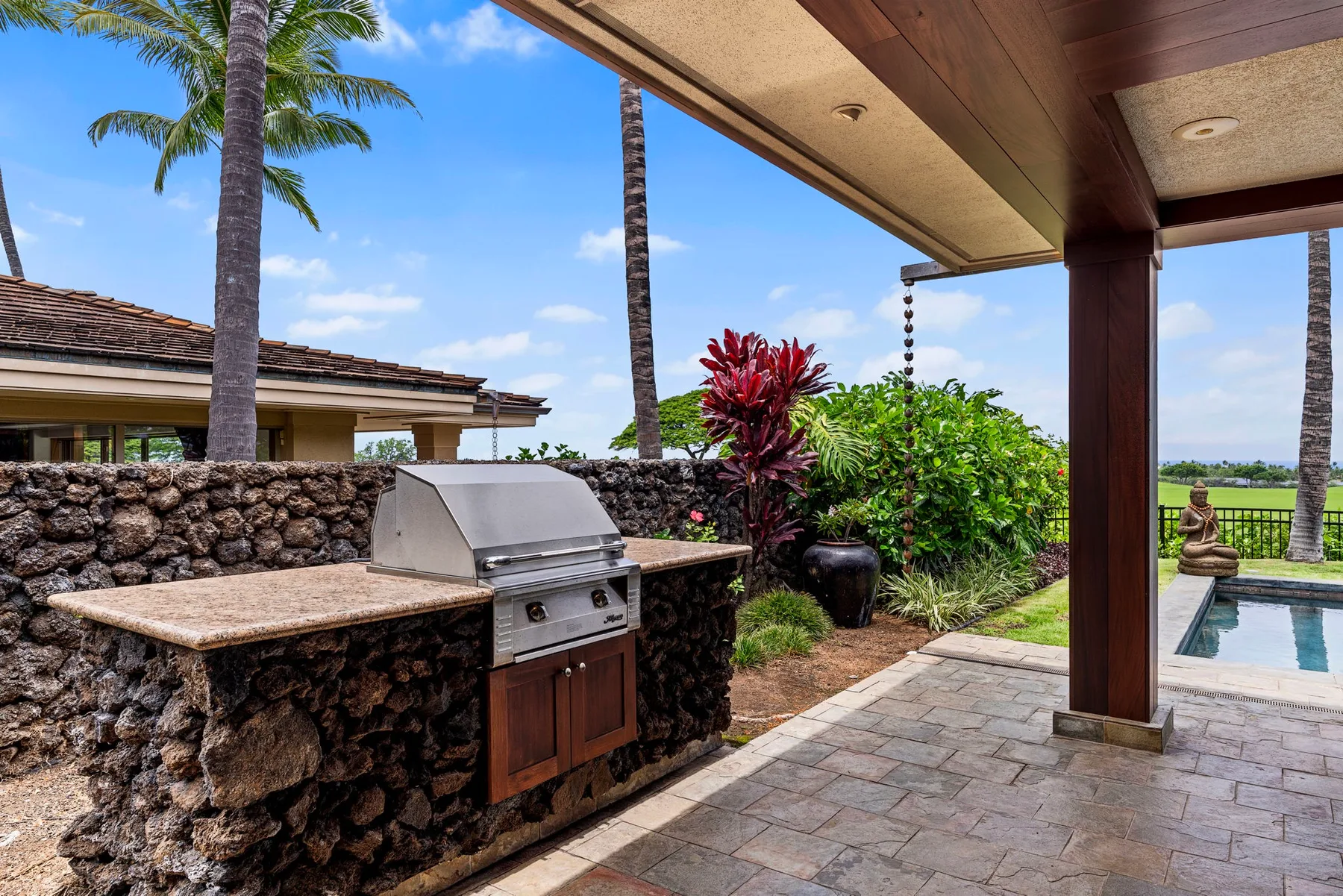 A covered outdoor patio features a built-in grill and a view of the pool.
