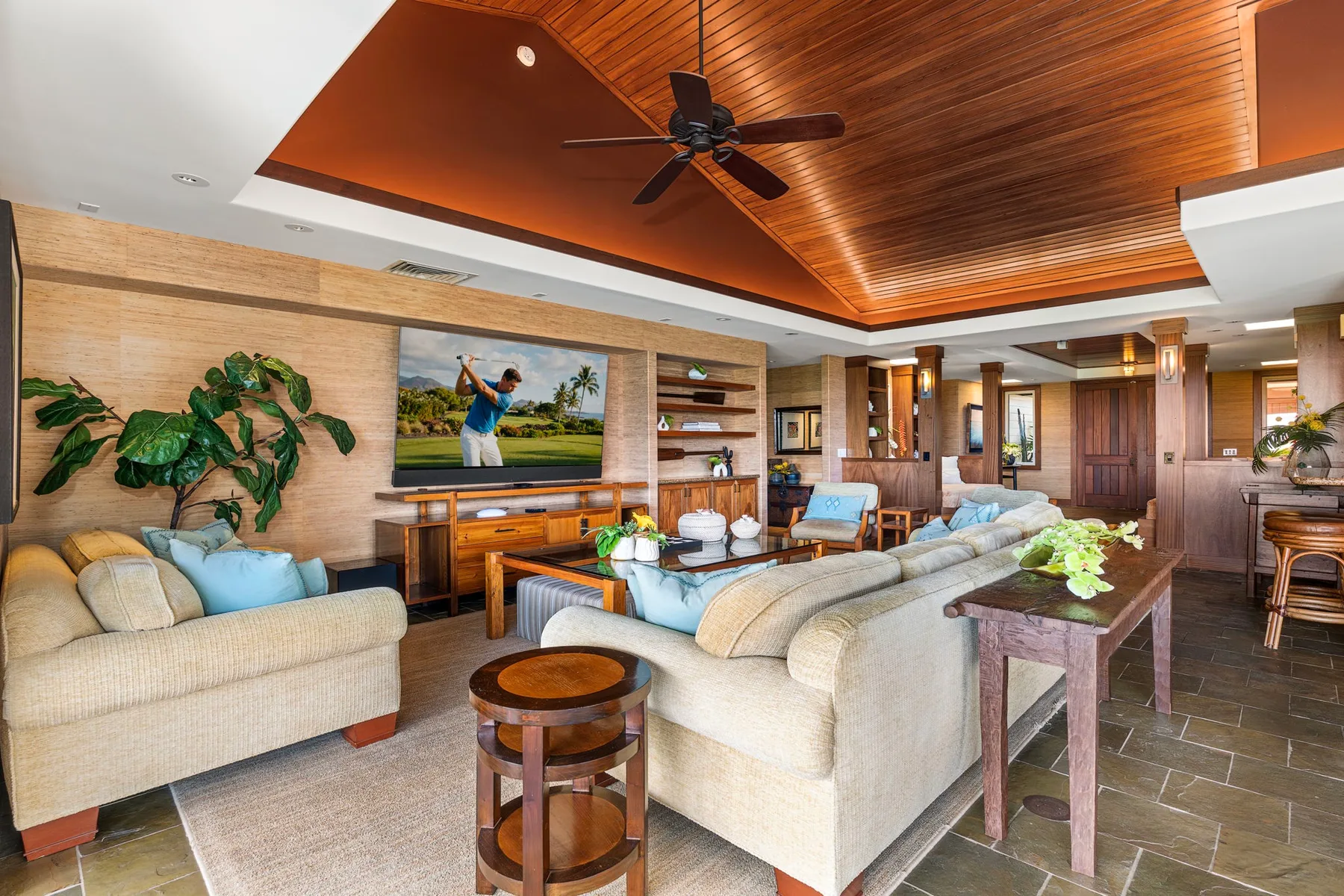 A living room with light-colored seating, a television, and a wood-paneled ceiling.