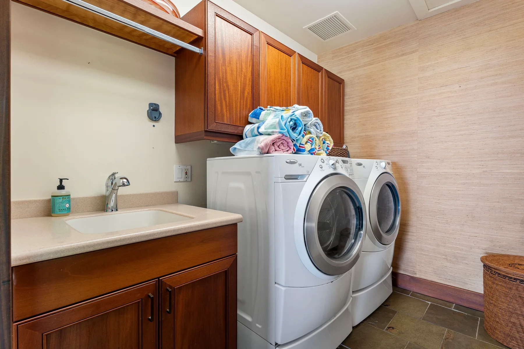 A laundry room with front-loading washing machines beside a sink and cabinets.
