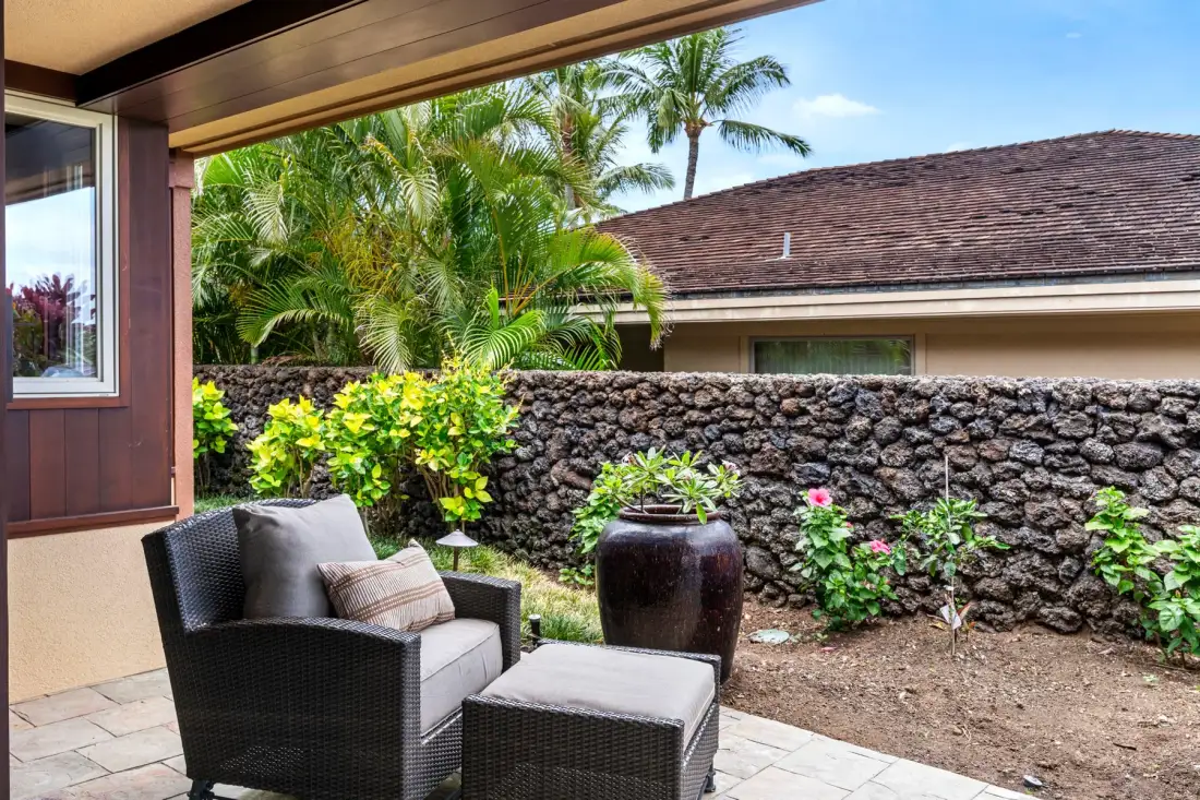 A covered patio seating area overlooks a stone wall and tropical greenery.