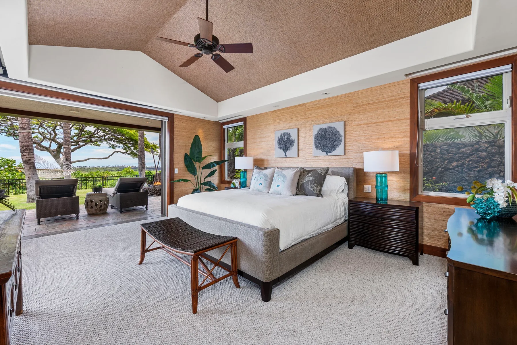 A bedroom with a bed, ceiling fan, and large windows overlooking greenery.