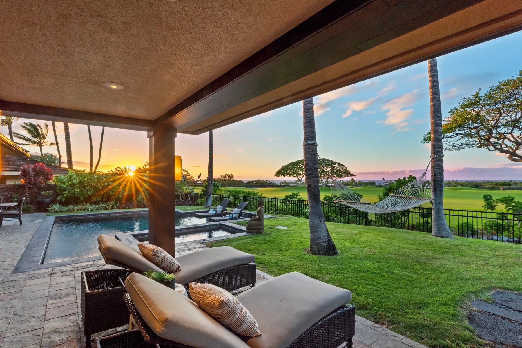 A covered patio with outdoor seating overlooks a green lawn and open landscape.