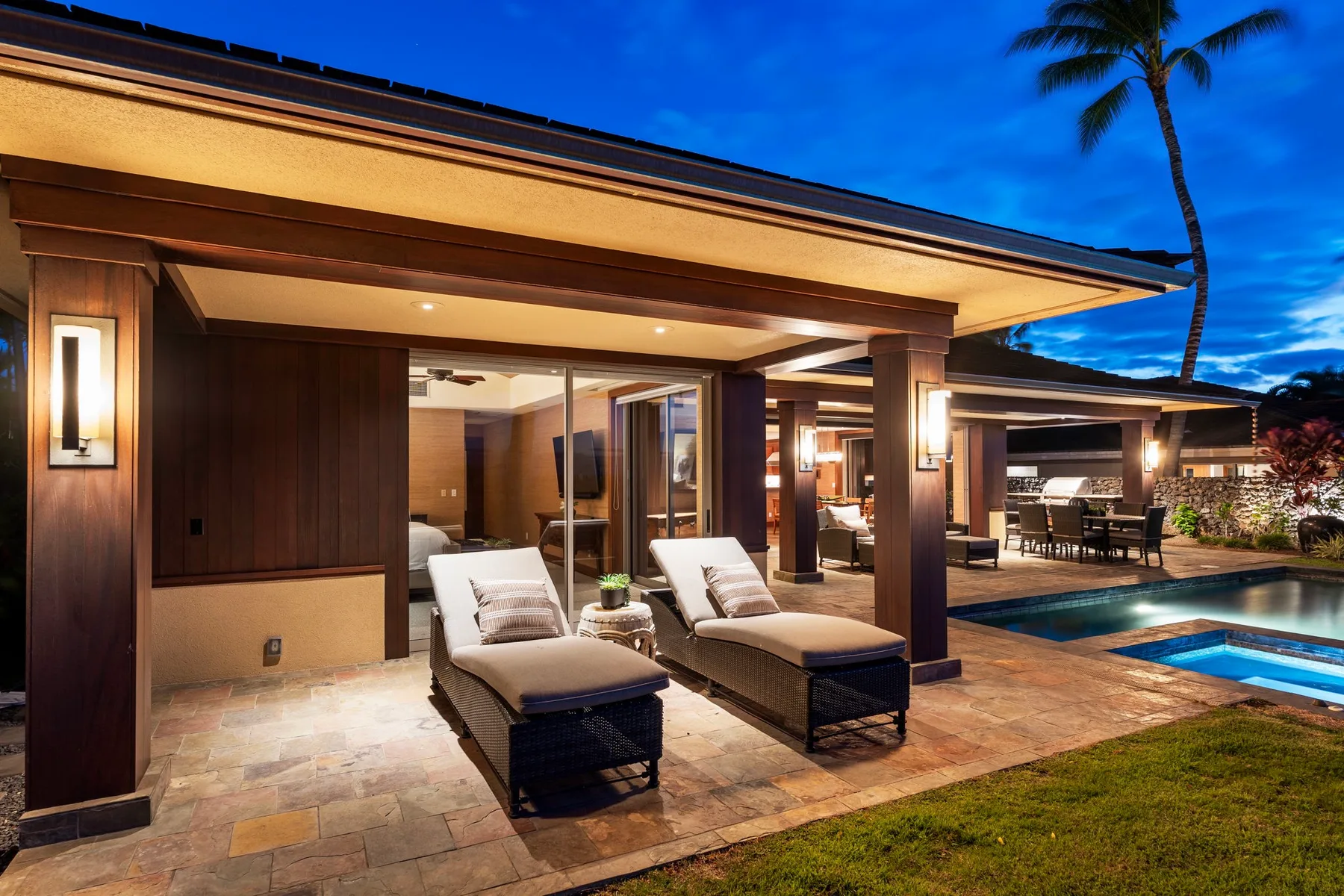 A covered patio with lounge seating overlooks a pool at dusk.