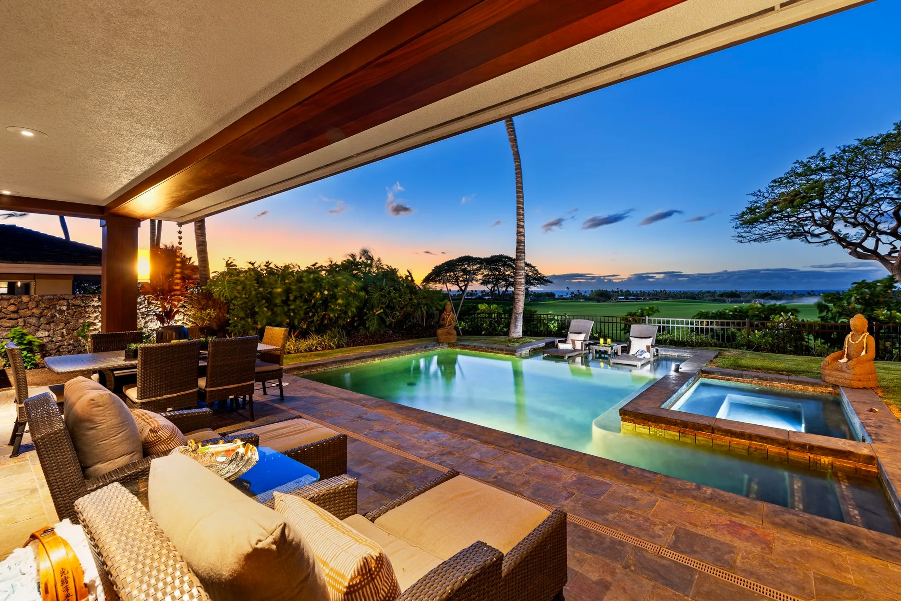 A covered patio overlooks a swimming pool and a scenic landscape at sunset.