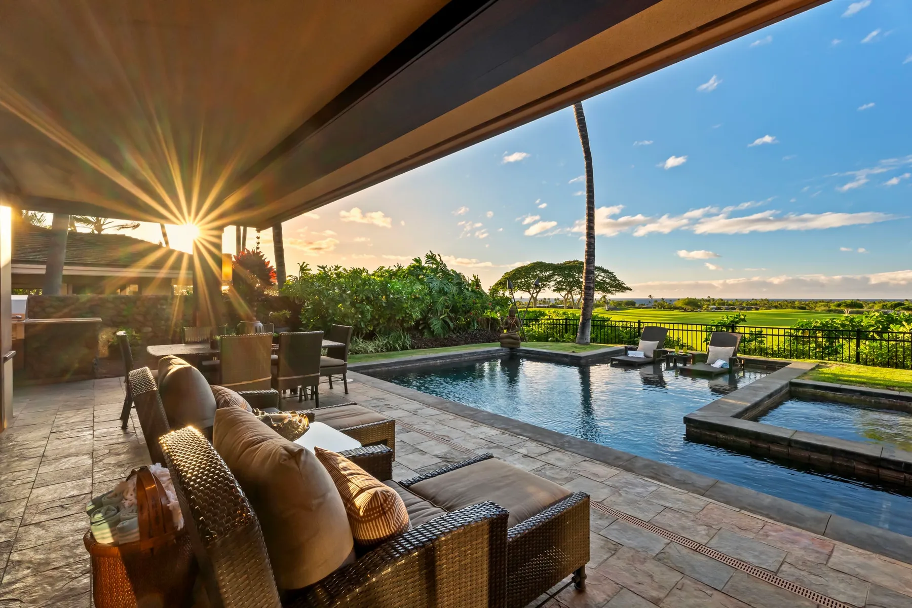 A patio with a swimming pool, outdoor seating, and a view of greenery.
