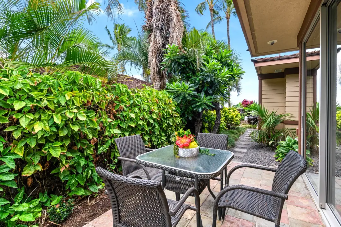 A patio seating area with a glass table and lush tropical plants.