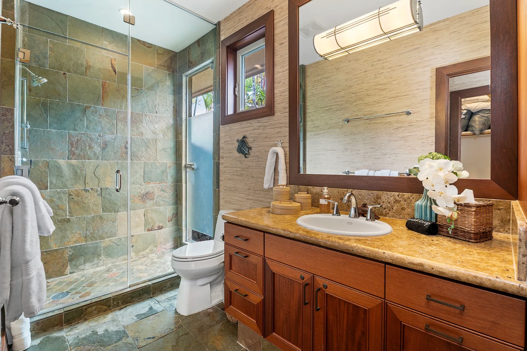 A bathroom with a glass shower, toilet, and wooden vanity.