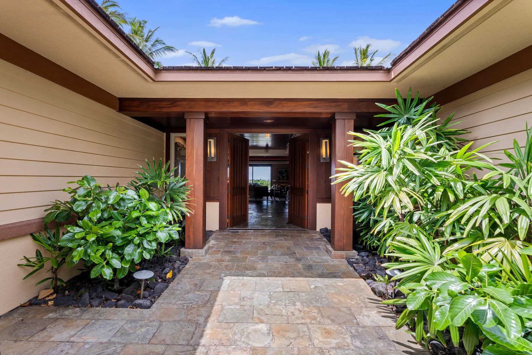 A stone-paved entrance courtyard framed by lush greenery and open to the sky.