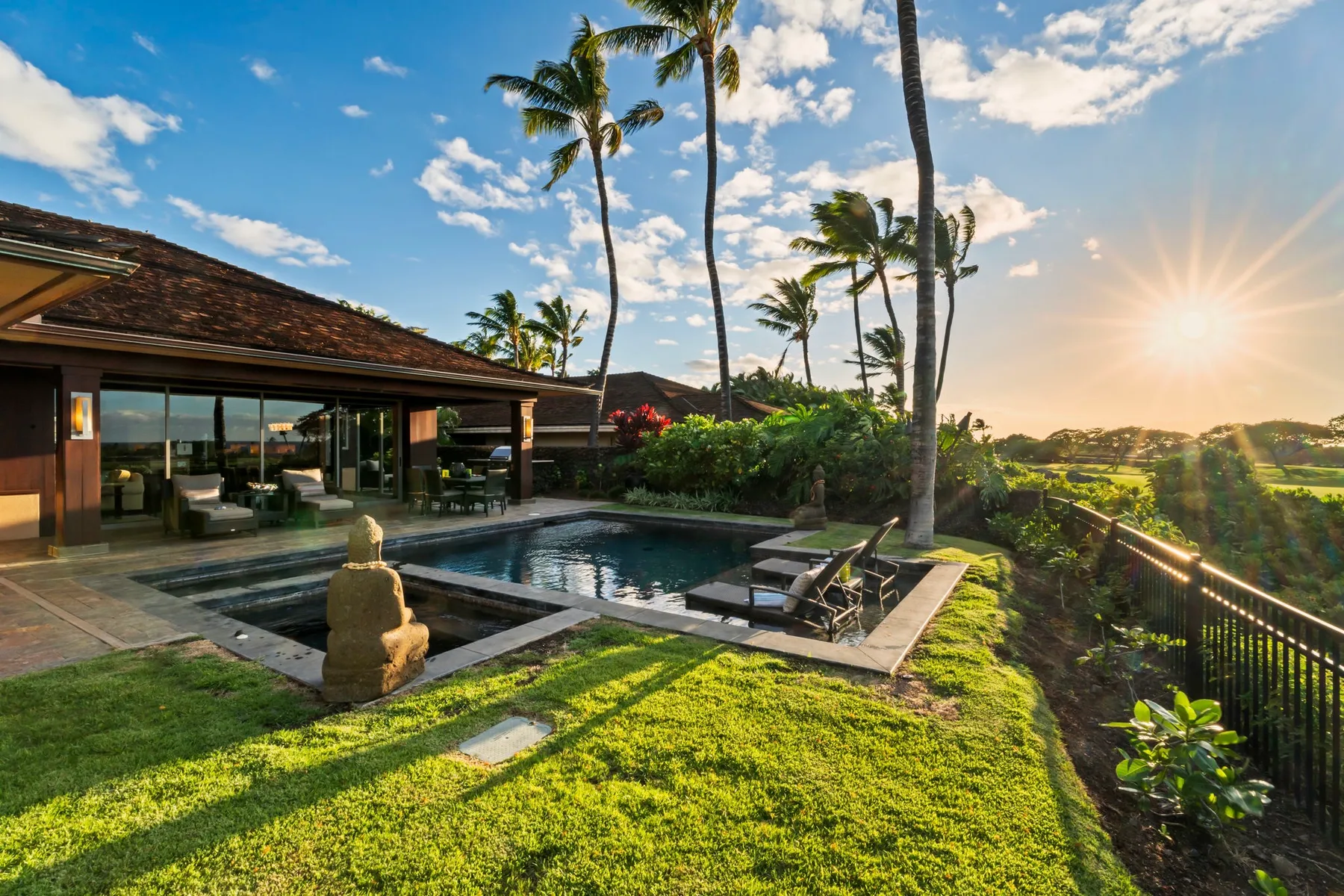 A tropical resort patio overlooks a pool surrounded by palm trees and greenery.