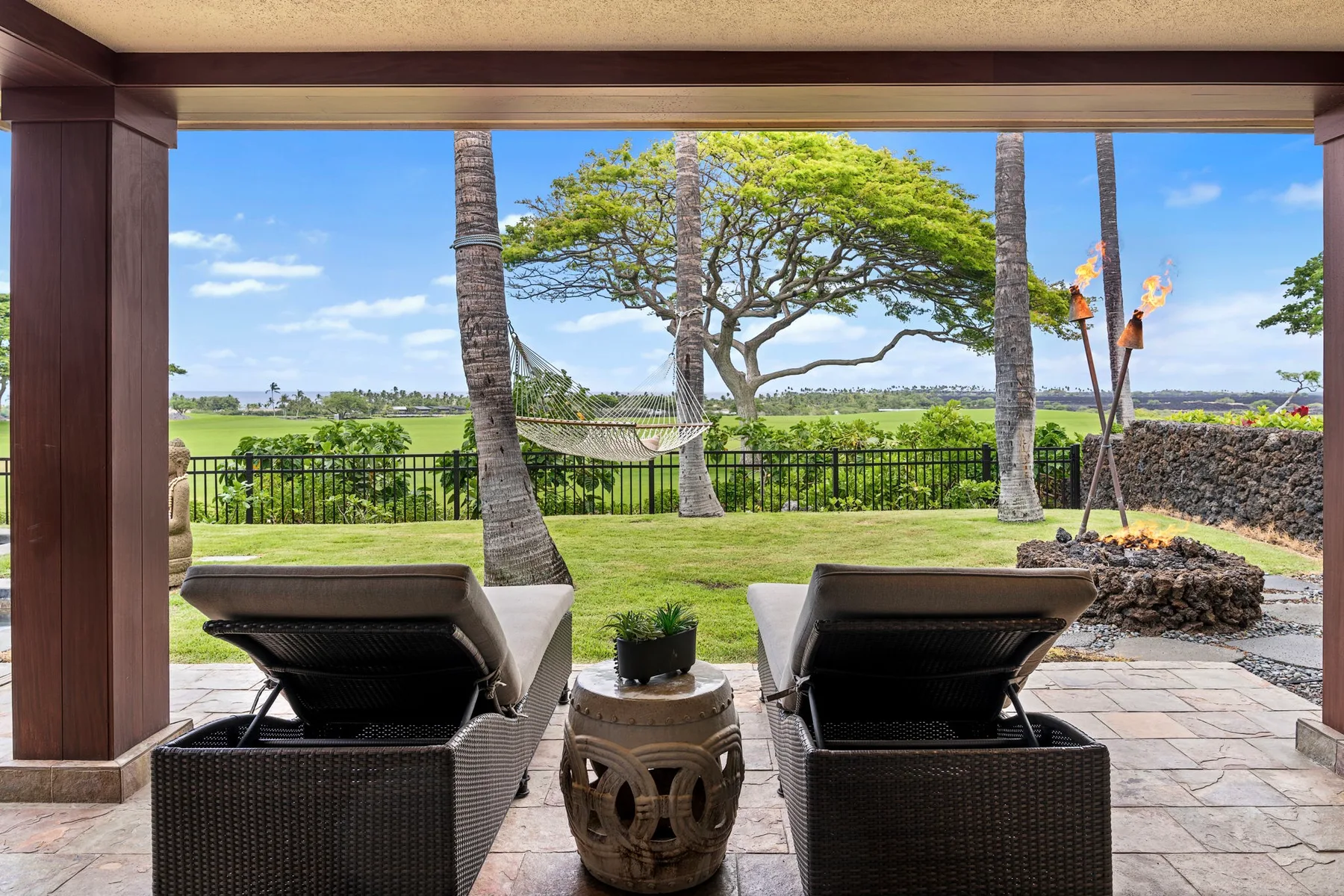 A covered patio with outdoor seating overlooks a green lawn and open landscape.