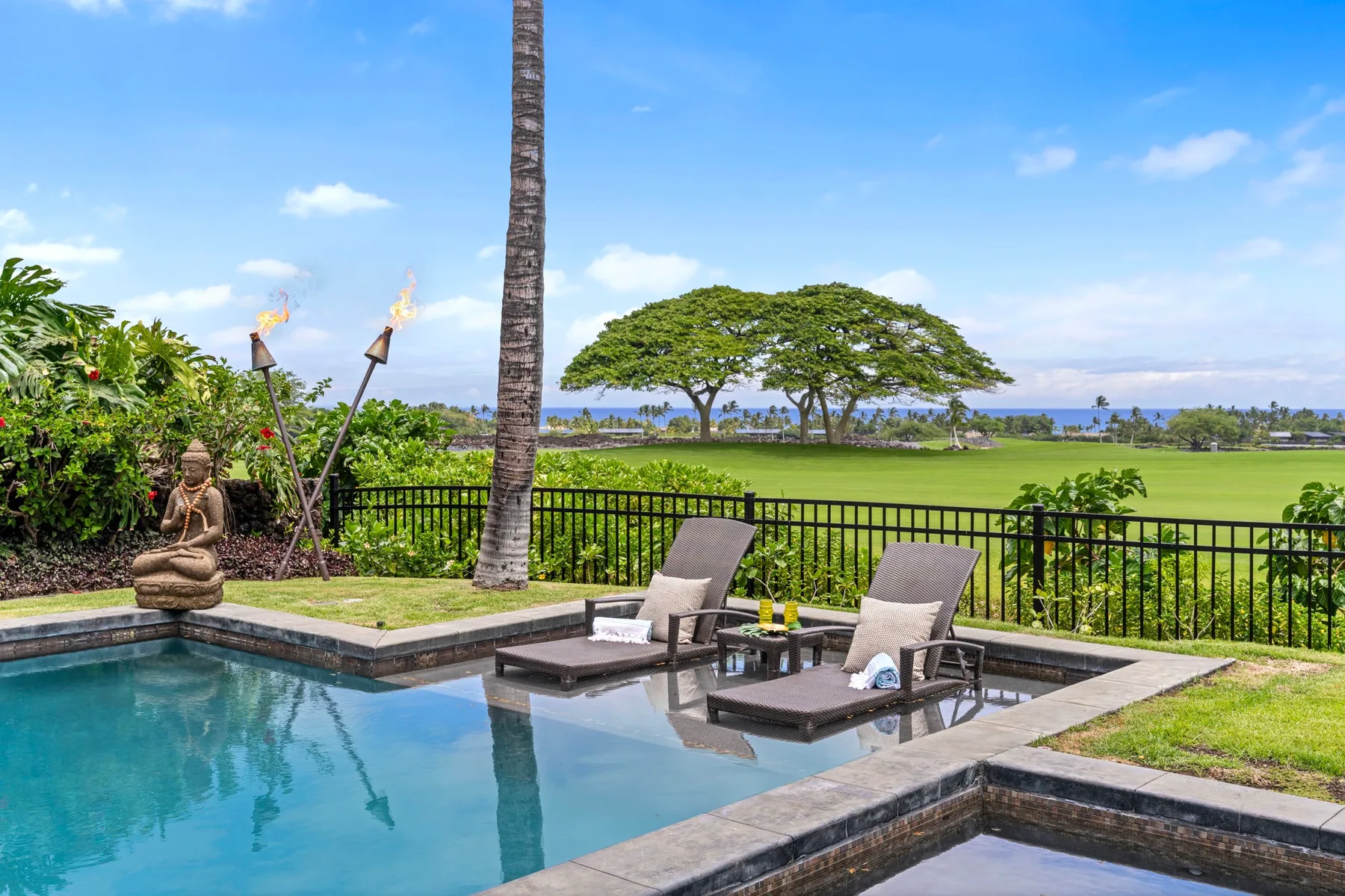 An outdoor poolside seating area overlooks a green lawn and distant water.