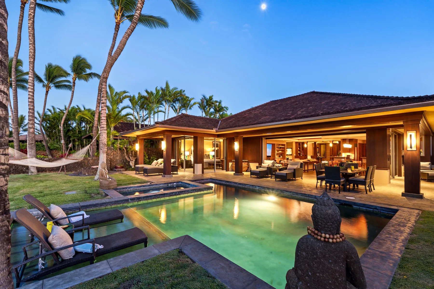 A tropical villa opens onto an illuminated swimming pool and outdoor seating.