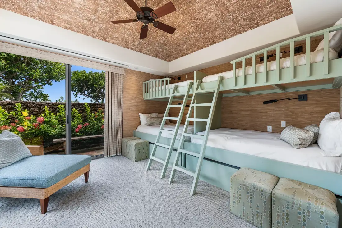 A bedroom with two elevated beds, a ladder, and a sliding glass door opening to greenery.
