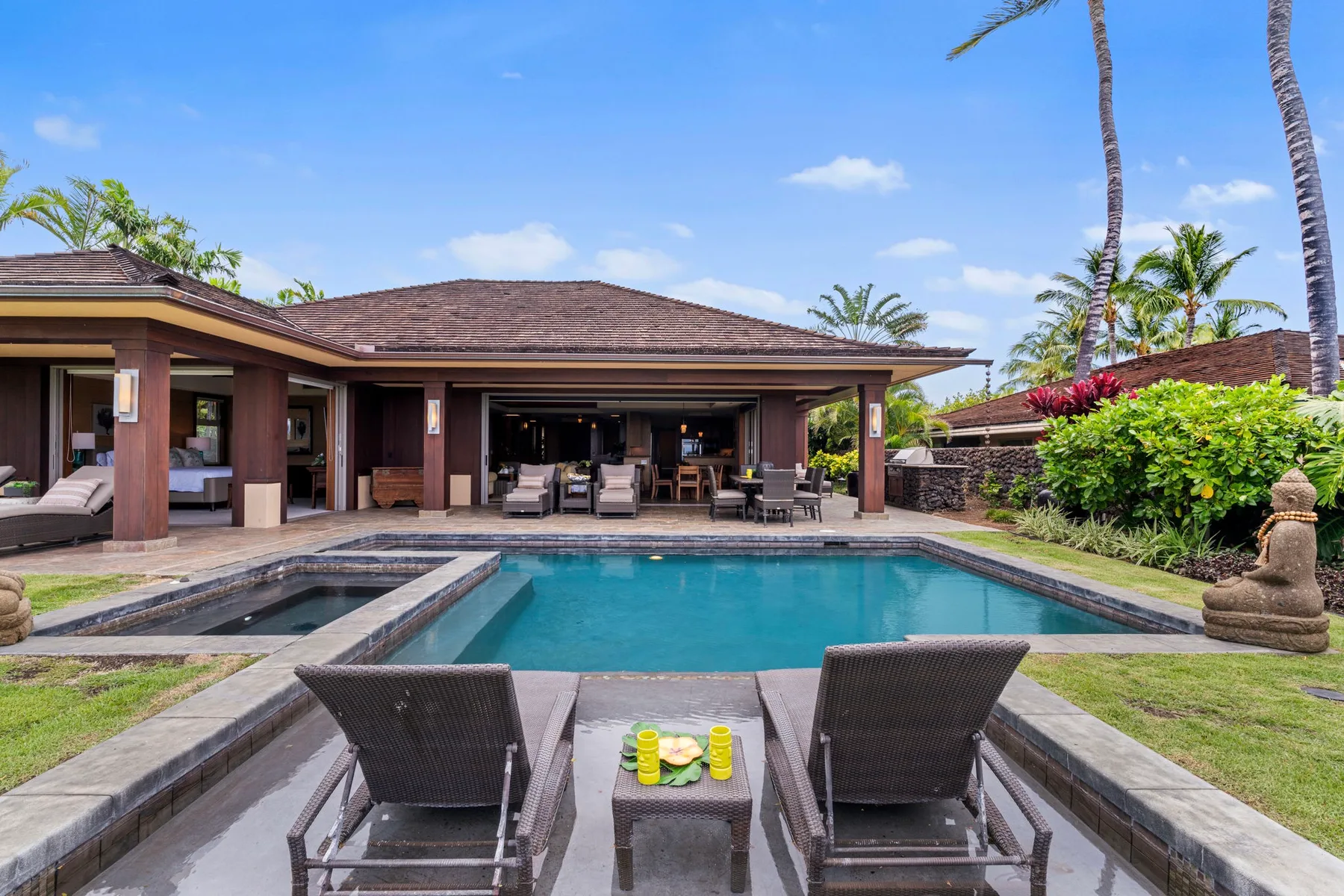 An outdoor swimming pool faces an open-sided patio with seating.