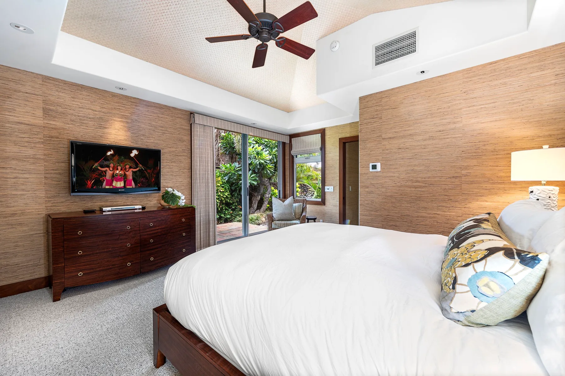 A bedroom with a bed, dresser, and glass doors opening onto greenery.