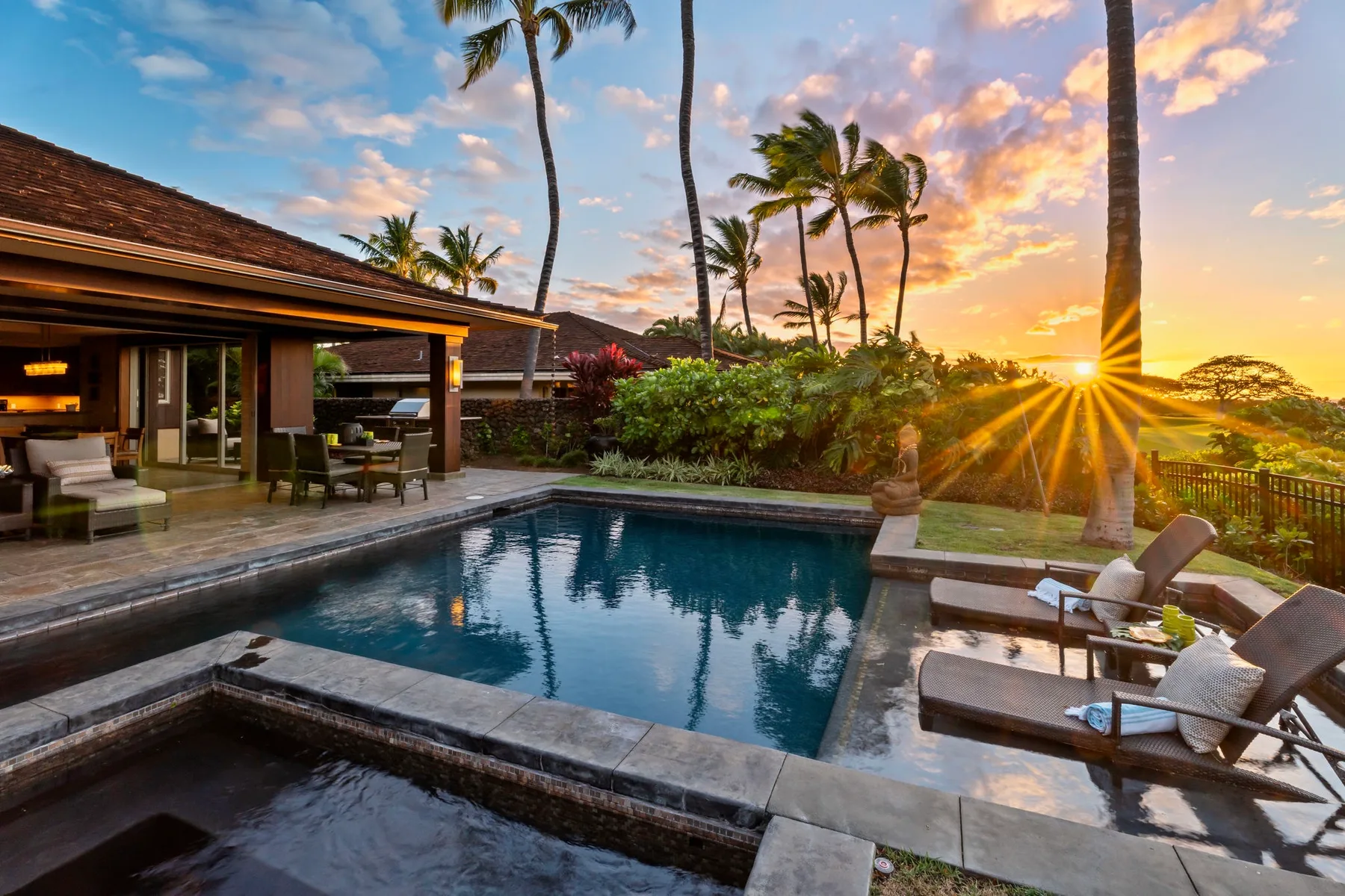 An outdoor pool beside a covered seating area, with palm trees at sunset.