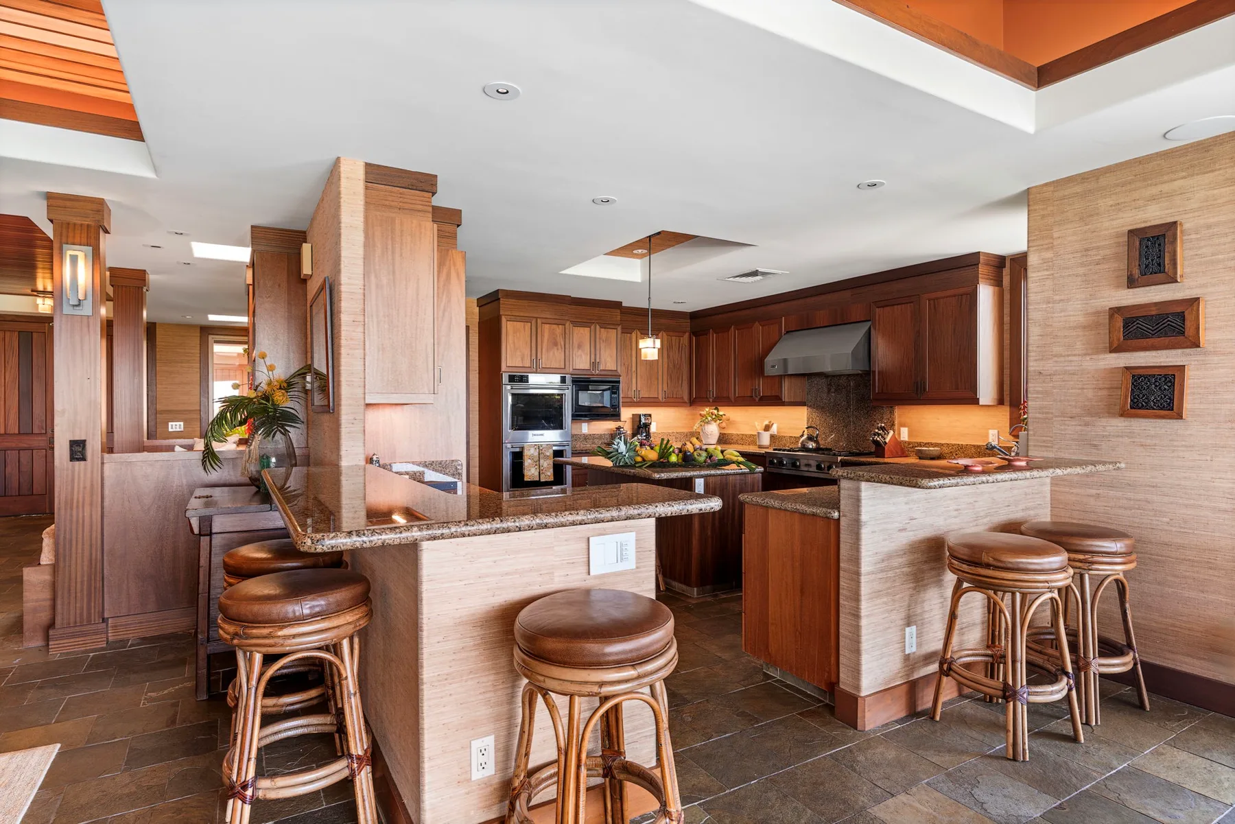 A spacious kitchen with wood cabinetry, stone counters, and bar seating.