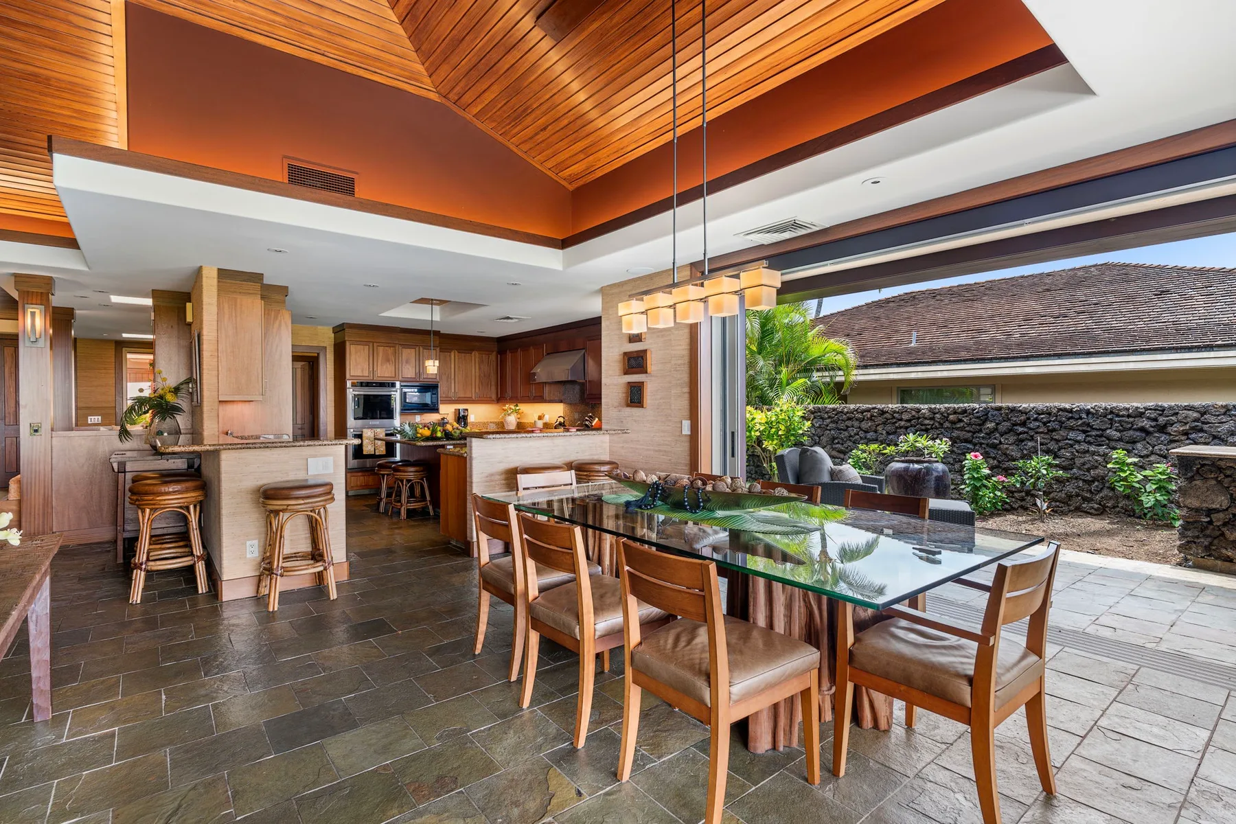 An open-plan kitchen and dining area with a long table beside a covered patio.