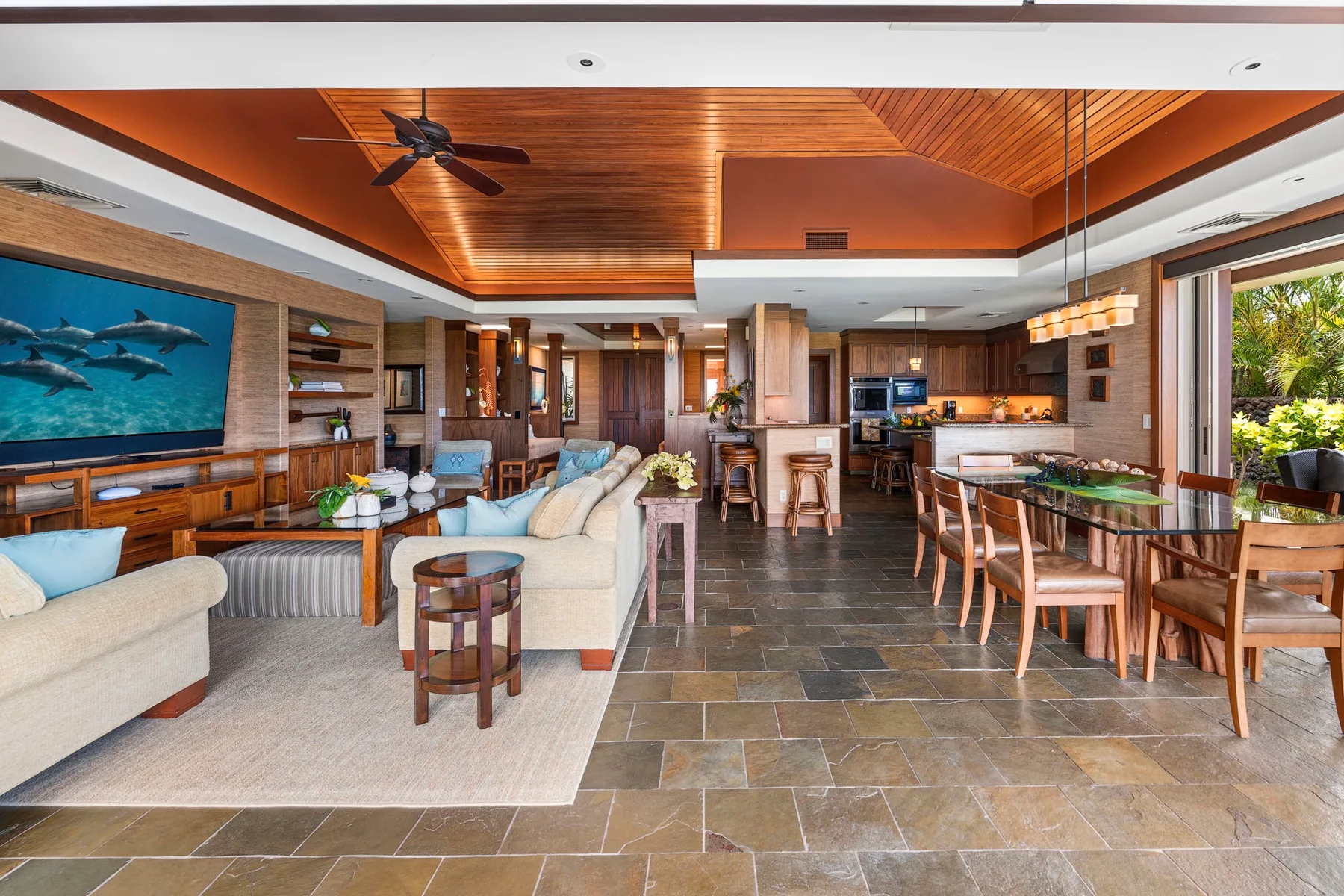 An open-plan living and dining area with a kitchen and wood-paneled ceiling.