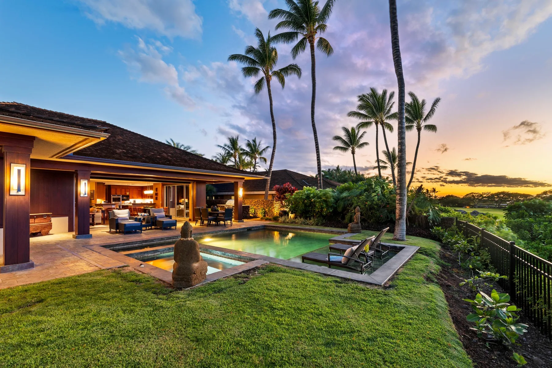 An outdoor pool and patio beside a tropical home at sunset.