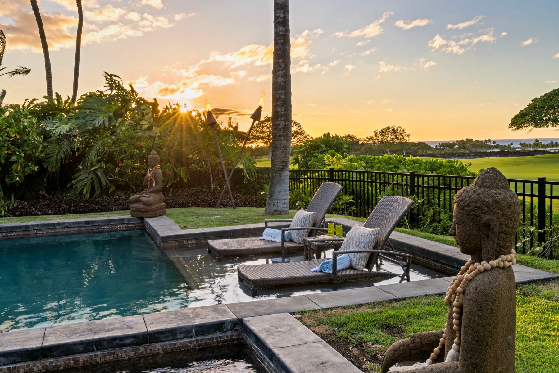 Outdoor poolside seating overlooks a landscaped garden and water at sunset.