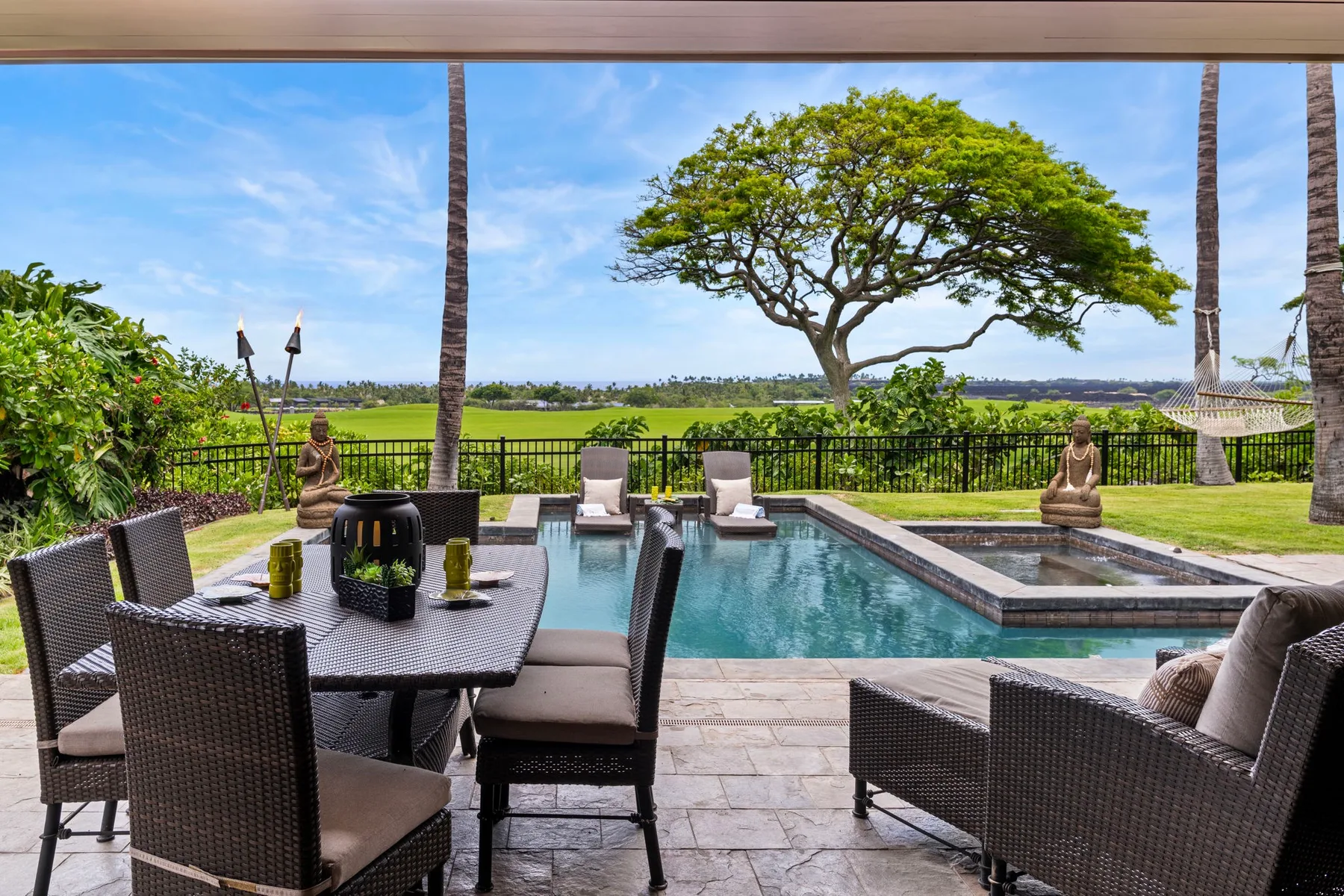An outdoor patio with dining seating overlooks a swimming pool and green landscape.