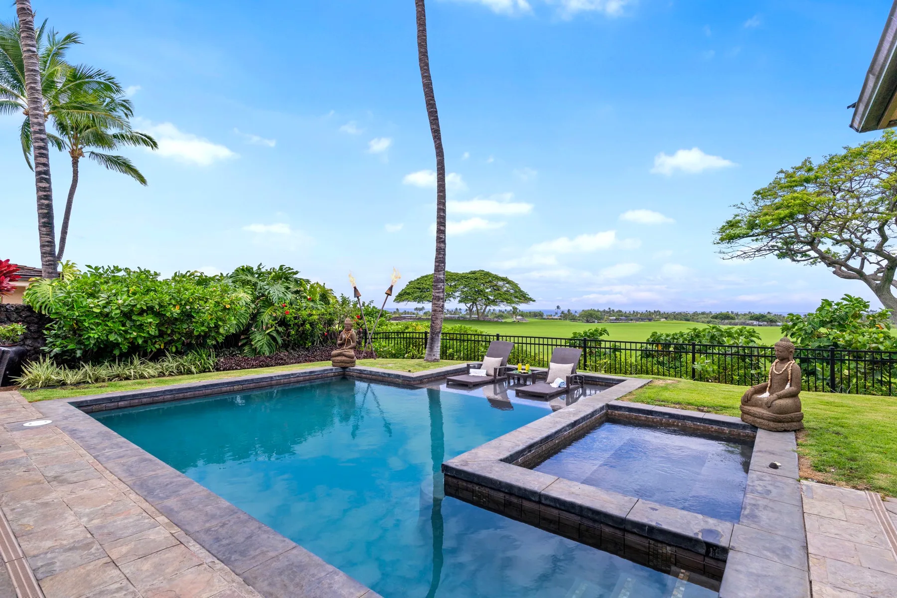 An outdoor pool beside a smaller shallow basin, with loungers and a green landscape beyond.