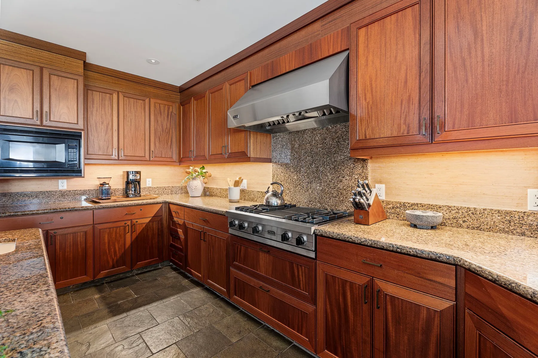 A kitchen with wooden cabinets, stone countertops, and a central cooktop.