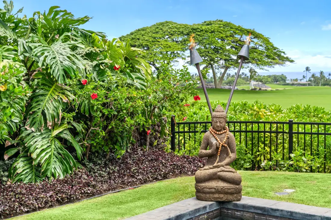 A landscaped garden with tropical plants, flowering shrubs, and a seated statue.