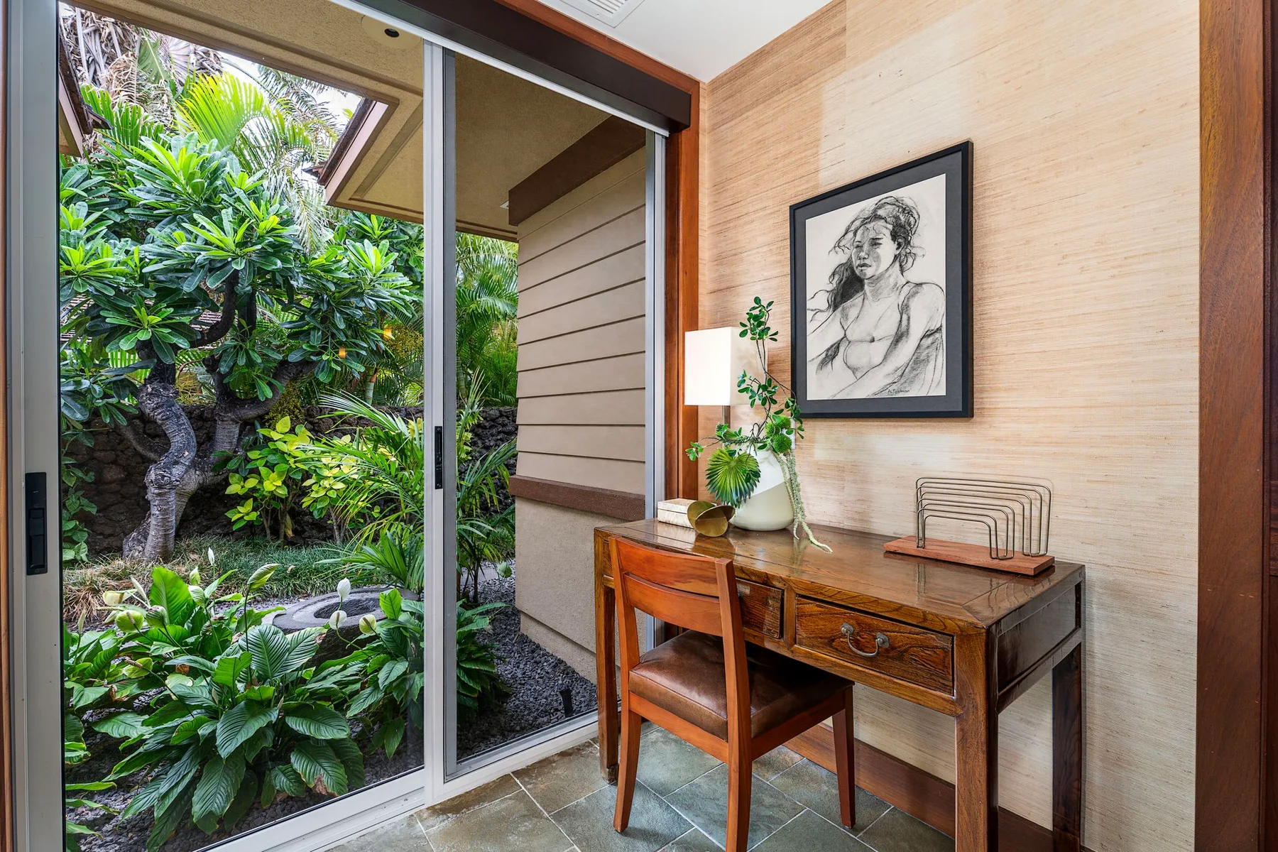 A small desk and chair sit beside sliding glass doors overlooking a leafy garden.