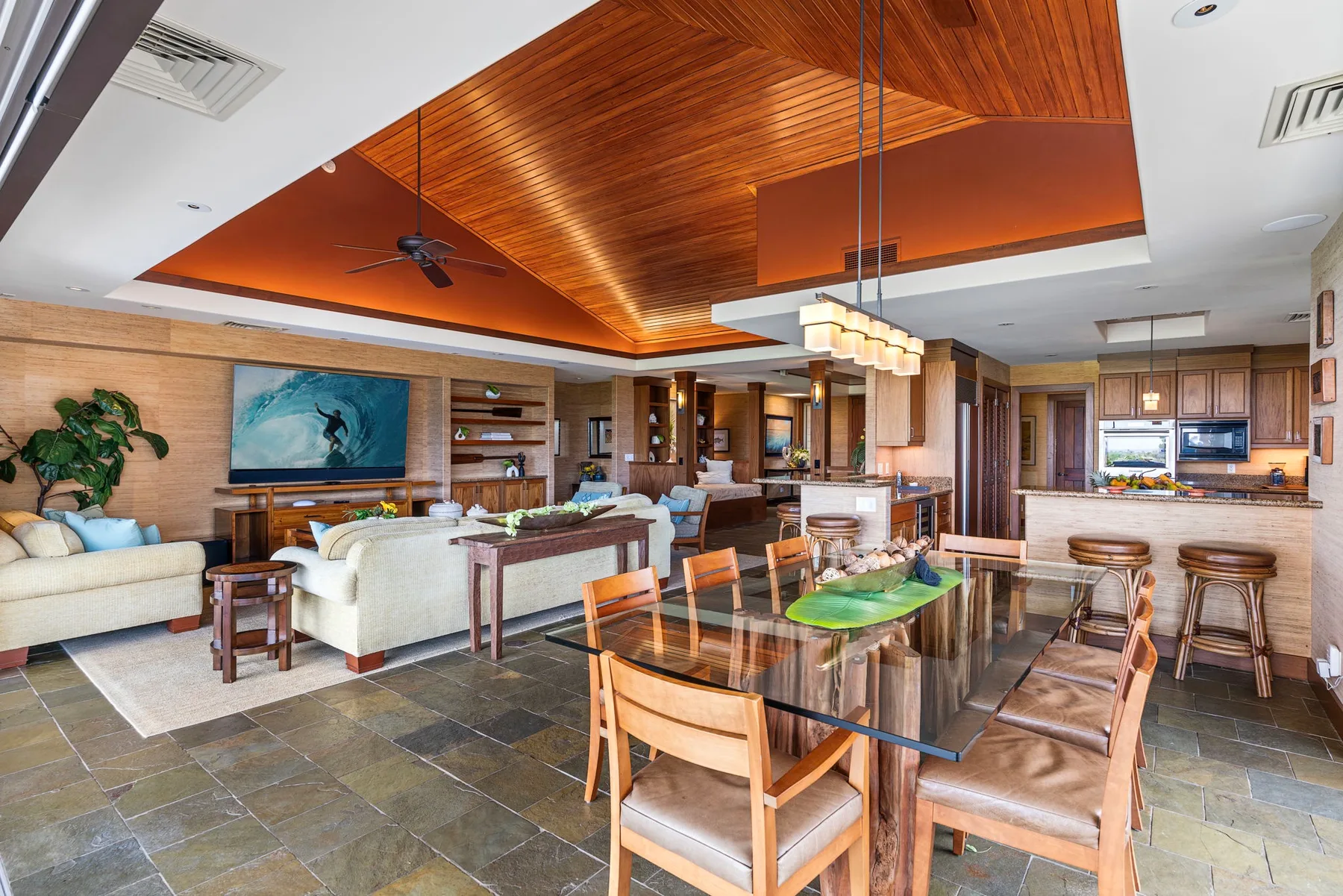 An open-plan living and dining area with a kitchen and a wood-paneled ceiling.