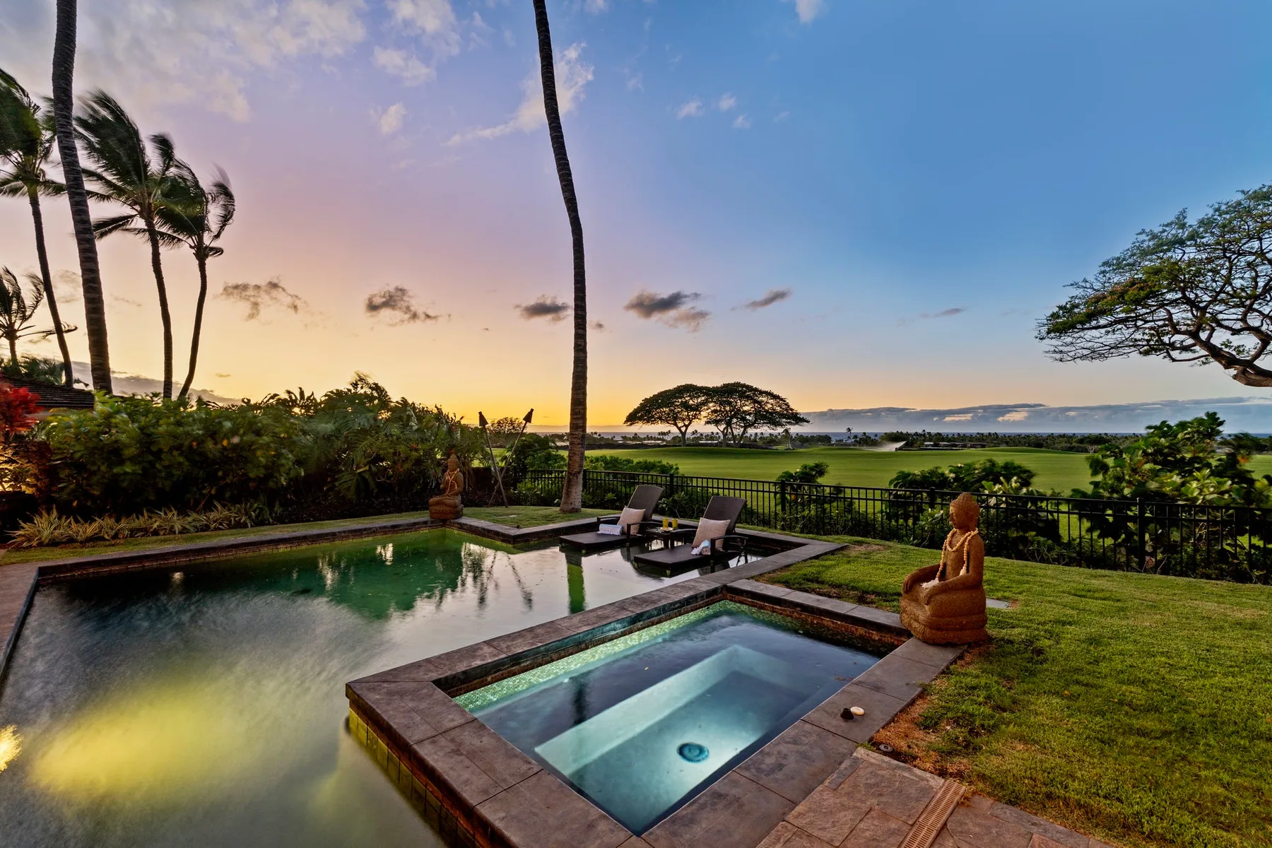 An outdoor pool and square spa overlook a landscaped lawn and distant water at sunset.
